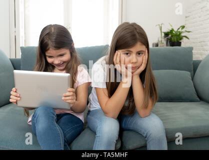 Sibling angry at younger sister spending too much time online using laptop. Digital technology addicted kid playing with computer ignoring her sad old Stock Photo