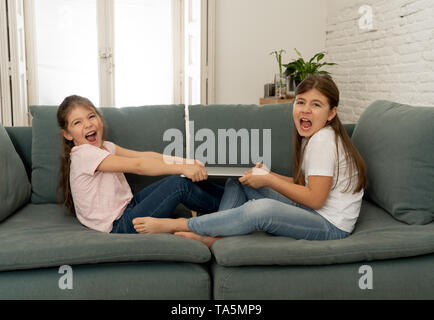 Younger and older girls fighting for laptop arguing over playing on the internet. Lifestyle portrait of sisters not sharing computer in Relationship b Stock Photo