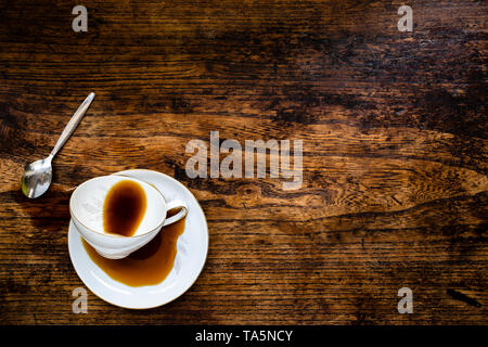 Spilled coffee next to a vintage cup on a dark woorden table Stock Photo