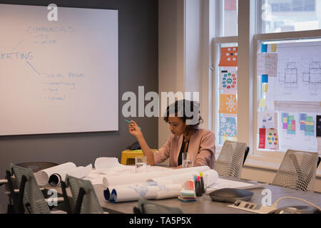 Female architect reviewing blueprints in conference room Stock Photo