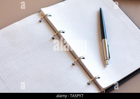 Open notebook with pen lying on it on beige desktop. Notepad sheets on silver brackets, automatic ballpoint pen in silver-black colour. Stock Photo