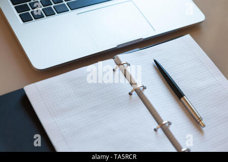 Top view on working space. Laptop and open notebook with pen on beige desktop. Notepad sheets on silver brackets, automatic ballpoint pen Stock Photo