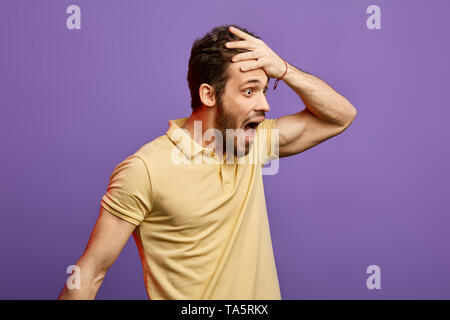 shocked man wearing yellow T-shirt loking aside , stunned with some incredible story, holding hands on forehead.Oh my God. what's a shame. happy man r Stock Photo