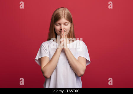 faithful kind woman with closed eyes in casula clothes prays for wellness of her family, keeps palms pressed together, poses in praying gesture agains Stock Photo