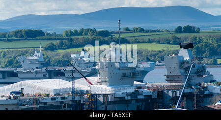 Rosyth, Scotland, UK. 22nd May, 2019. Aircraft carrier HMS Queen Elizabeth moored off Rosyth in the River Forth after leaving dry dock yesterday after a visit to her home port. She will leave the Forth today and return to sea in preparation for Westlant 19 deployment which is designed to focus on the operations of her F-35 fighter aircraft. Pictured; Rare view of both of the Royal Navy's aircraft carriers. HMS Queen Elizabeth and in foreground HMS Prince of Wales still under construction in shipyard at Rosyth. Credit: Iain Masterton/Alamy Live News Stock Photo