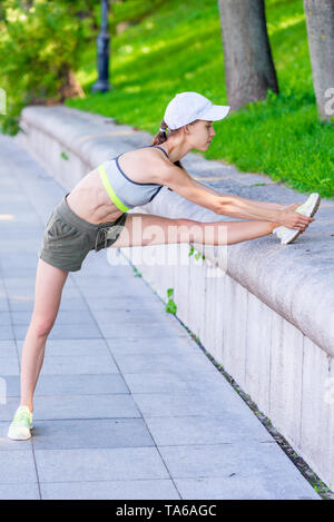 exercises on the city embankment, a female athlete stretches and warms up her muscles before jogging Stock Photo