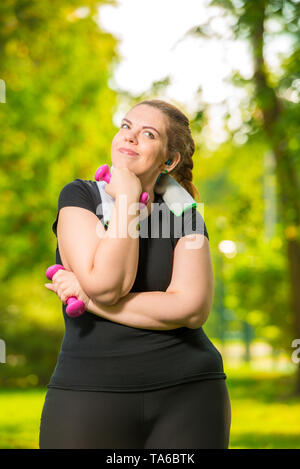 dreaming about slim body model plus size is engaged with dumbbells during a workout in a summer park Stock Photo