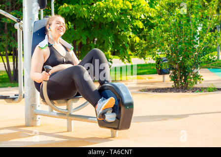 happy and active oversized woman doing exercise on a stationary bike in a city park Stock Photo