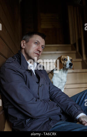 Mature man and beagle are sitting on wooden stairs and looking away. Stock Photo