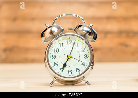 Silver alarm clock in retro style on a wooden background close-up shows 7 am Stock Photo