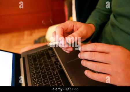 Man working on a laptop at home office, hand typing on keyboard with a cigarette in his hand is holding and smoking, close up. Using notebook computer Stock Photo