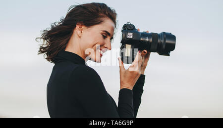 Professional female photographer with dslr camera photographing. Young woman with camera taking pictures outdoors. Stock Photo