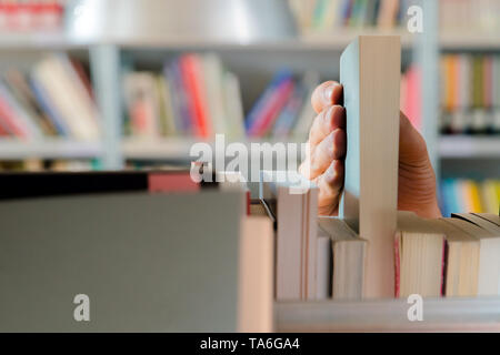 Young student picking a book from the shelf in the library. Preparing for exams, young man searching for or choosing a book in the public library in u Stock Photo