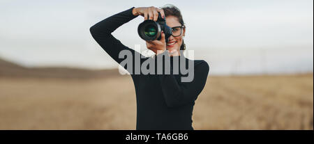 Professional female photographer with dslr camera photographing outdoors. Young woman with camera taking pictures. Stock Photo