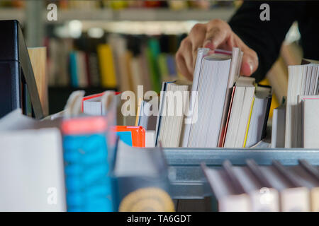 Young student picking a book from the shelf in the library. Preparing for exams, young man searching for or choosing a book in the public library in u Stock Photo