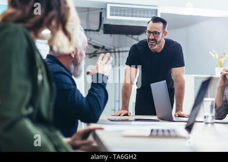Happy mature businessman talking with colleagues during a meeting. Smiling male professional discussing new ideas with team. Stock Photo