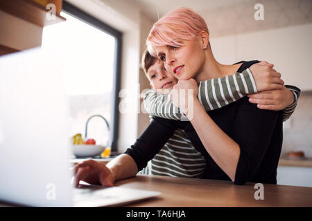 A young woman with a small son using laptop in a kitchen at home. Stock Photo