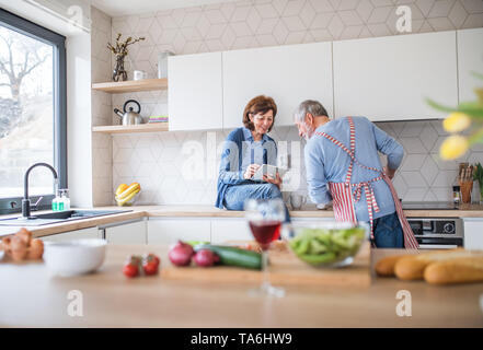 A portrait of senior couple in love indoors at home, using tablet. Stock Photo