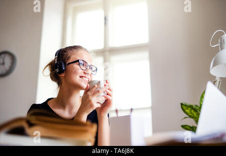 A young female student sitting at the table, using headphones when studying. Stock Photo