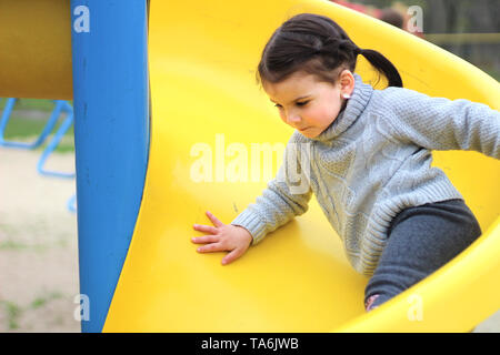 Hispanic Girl Sliding Down Outdoor Slide With Arms Raised Above