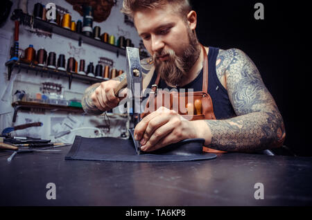 Leather Currier cutting out leather shapes for a new product in his tanning shop Stock Photo