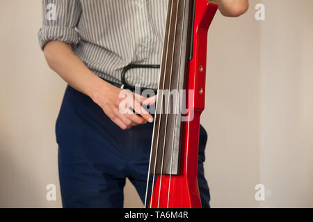 Man plays red modern electric contrabass in musical studio Stock Photo