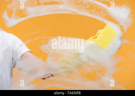 cropped view of cleaner in rubber glove cleaning glass with sponge on orange background Stock Photo