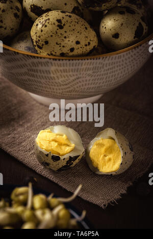 Vertical photo of single boiled quail egg broken in the middle. Other quail eggs are in bowl in background. eggs are placed on wooden board with mung  Stock Photo