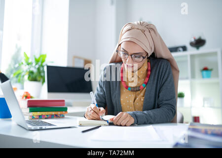 Busy Muslim teacher sitting at the table with books and working Stock Photo