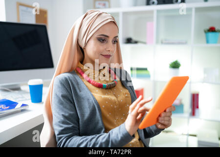 Beautiful Muslim woman with nice makeup using her orange tablet Stock Photo