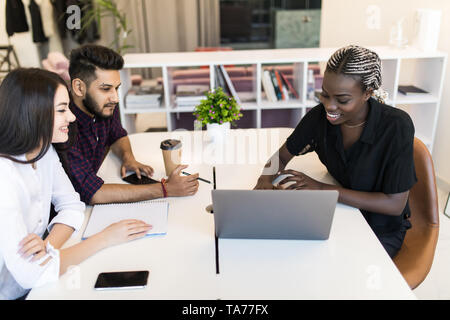 Serious african team leader explaining online project on laptop to diverse coworkers, focused three office workers planning work together listening to Stock Photo