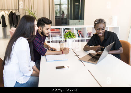 Serious african team leader explaining online project on laptop to diverse coworkers, focused three office workers planning work together listening to Stock Photo