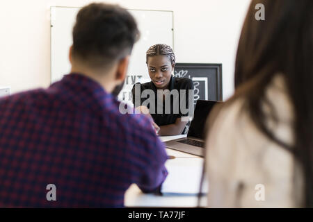 Three attractive, elegant, stylish businesspeople sitting in workplace, beautiful woman showing presentation on tablet to her partner, handsome man in Stock Photo