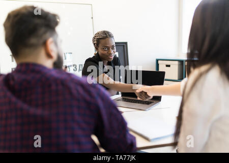 Three attractive, elegant, stylish businesspeople sitting in workplace, beautiful woman showing presentation on tablet to her partner, handsome man in Stock Photo