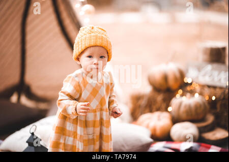 Cute baby girl 1-2 year old wearing yellow knitted hat and dress over lights at background. Stock Photo