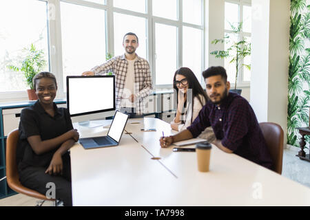 Young multiracial team and leader or coach looking at camera, smiling, standing near office desks in coworking space, posing for company business port Stock Photo