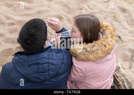 A couple sits in the sand and toast with champagne glasses Stock Photo