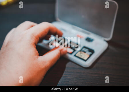 Hand picking SD card in a plastic storage box on the wooden table to be put in portable electronic devices like camera or camcorder Stock Photo