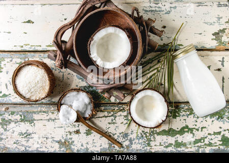 Variety of coconut products milk in glass bottle, oil and flakes in shell, fresh broken coconut on old wooden plank background. Healthy eating. Flat l Stock Photo