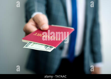 closeup of a young caucasian businessman, wearing an elegant gray suit, with his passport in his hand, with a 20 dollars banknote in it Stock Photo