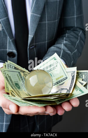 closeup of a young caucasian businessman wearing an elegant gray suit, with a pile of dollar bills and a crystal ball in his hands Stock Photo