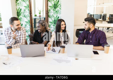 Diverse young and senior office workers collaborating and talking, multiracial employees working on computers. Staff discussing ideas projects sharing Stock Photo