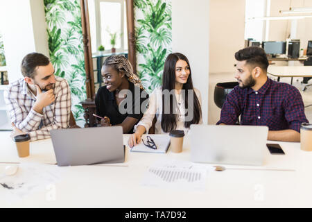 Diverse young and senior office workers collaborating and talking, multiracial employees working on computers. Staff discussing ideas projects sharing Stock Photo