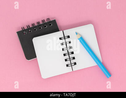 Two notebooks on a pink background with a blue pencil, top view. Stock Photo