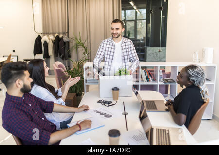 Company l members gathered in office greeting newcomer man employee. New worker holds carton box with personal belongings starting career in company f Stock Photo