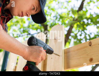 Young handsome man using electric drill on wooden fence Stock Photo