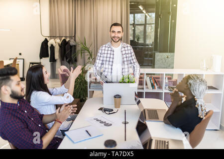 Company l members gathered in office greeting newcomer man employee. New worker holds carton box with personal belongings starting career in company f Stock Photo