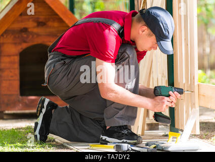 Young handsome man using electric drill on wooden fence Stock Photo