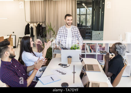 Company l members gathered in office greeting newcomer man employee. New worker holds carton box with personal belongings starting career in company f Stock Photo