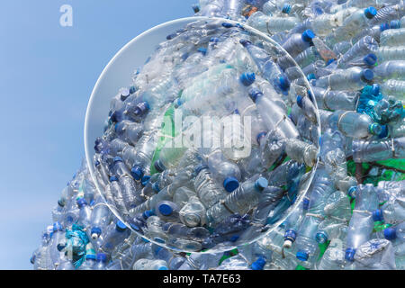 A lot of plastic waste bottles with a beautiful blue sky in the background and a transparent globe on the foreground Stock Photo